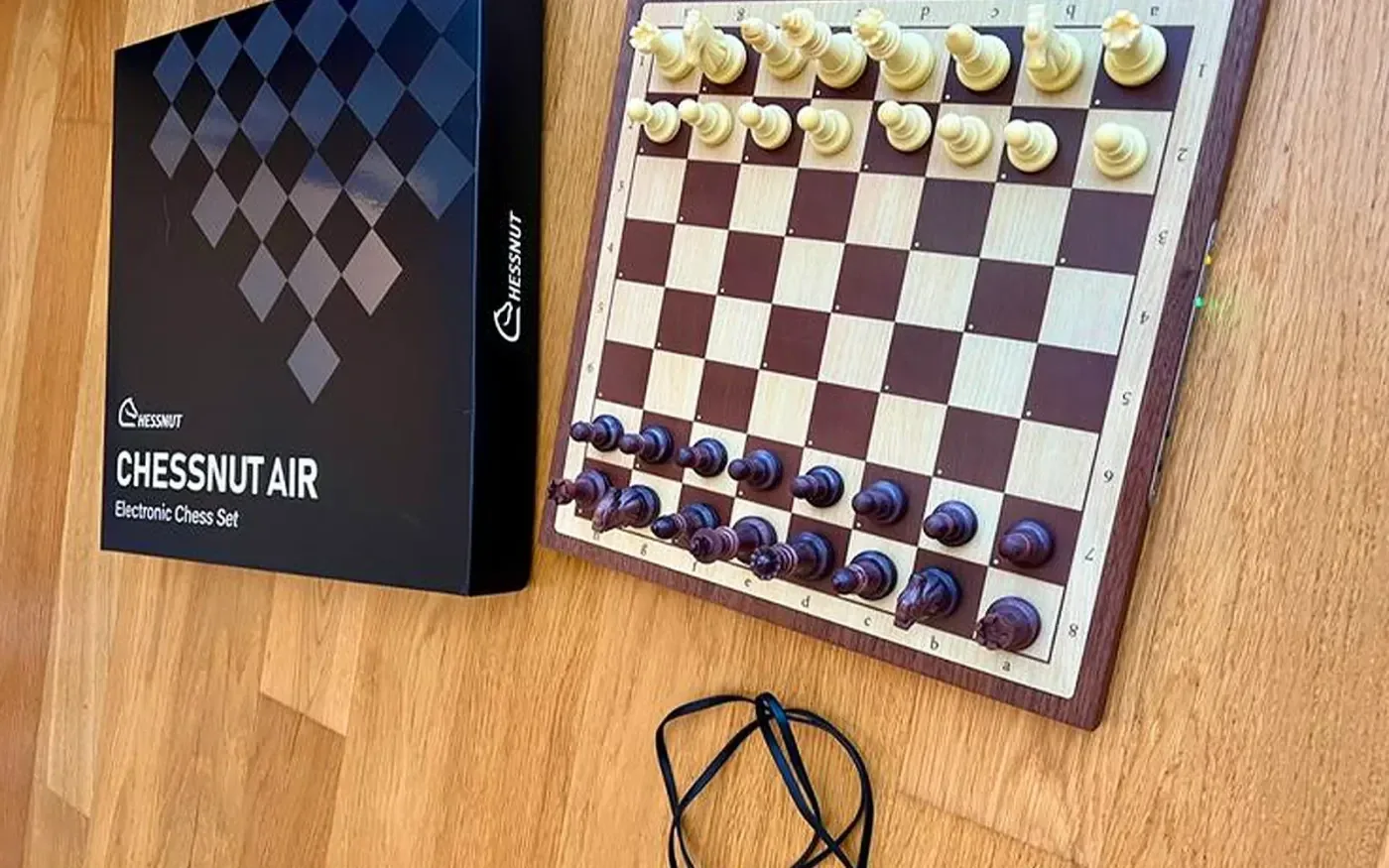 Коробка Chessnut Air и шахматная доска с комплектными светлыми и тёмными пластиковыми фигурами на деревянном столе